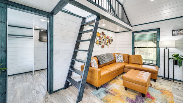 A modern living room with a sectional sofa, a colorful rug, and a wooden ladder.
