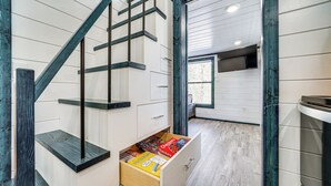 A modern interior with a wooden staircase, a drawer with various items, and a window providing natural light.