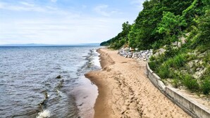 En strand med en gångbana av betong som löper längs strandkanten, omgiven av grönska.