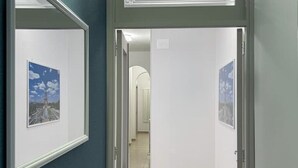 Un couloir aux murs ornés de tableaux encadrés, une porte donnant sur une autre pièce et un sol carrelé.
