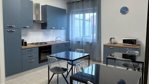 Une cuisine compacte dotée d’appareils électroménagers modernes, un coin repas avec une table et des chaises, et une fenêtre avec des rideaux.
