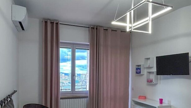 Une chambre d’hôtel comprenant un lit, un bureau, une chaise, une fenêtre avec des rideaux, un téléviseur fixé au mur et un radiateur.