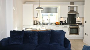Une cuisine moderne avec des meubles blancs, une cuisinière noire et un coin repas doté d’une table ronde prévue pour quatre personnes.