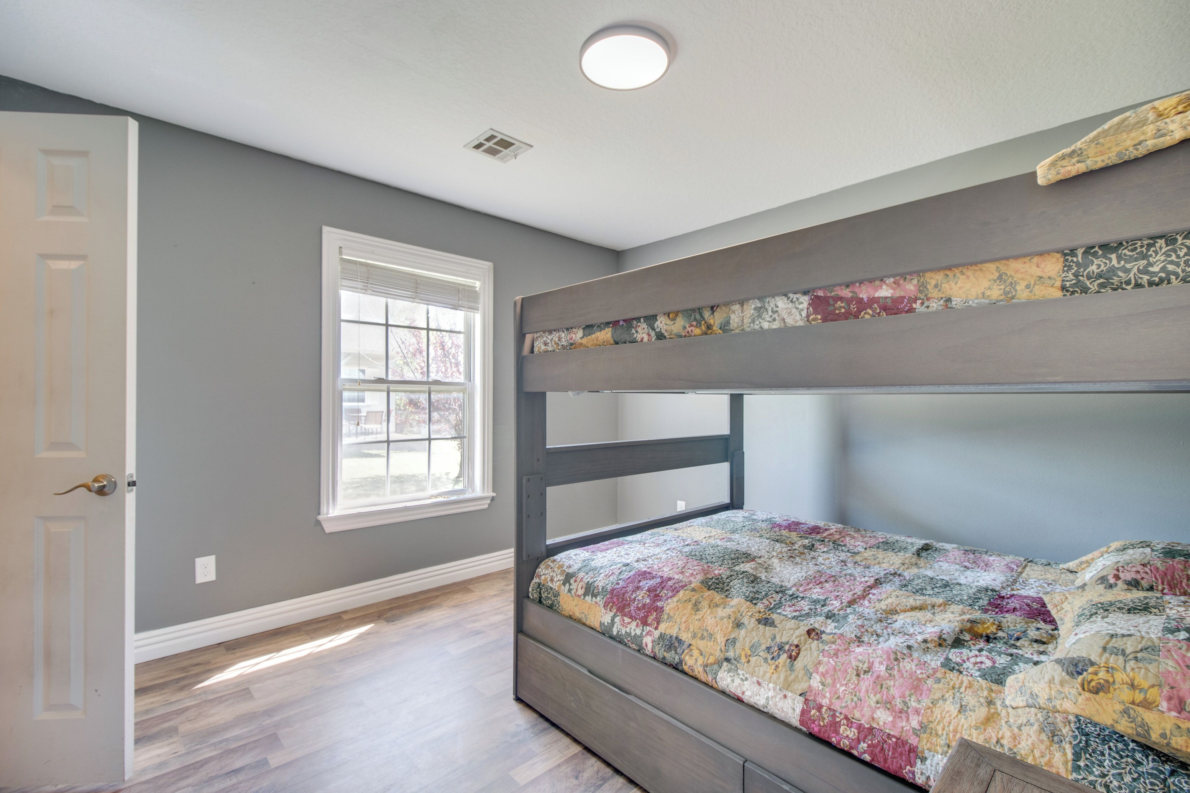 A room with a bunk bed, a window with blinds, and a door.