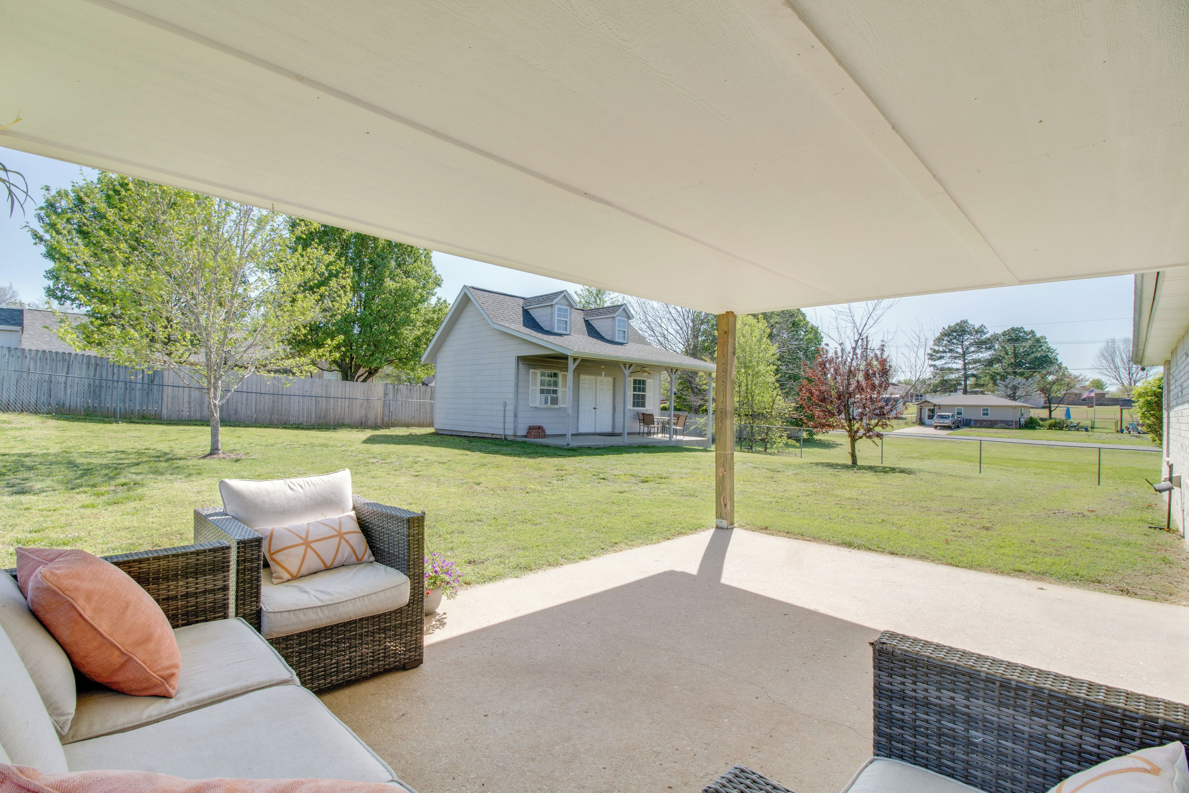 A covered patio area with wicker furniture and a view of a house in the background.
