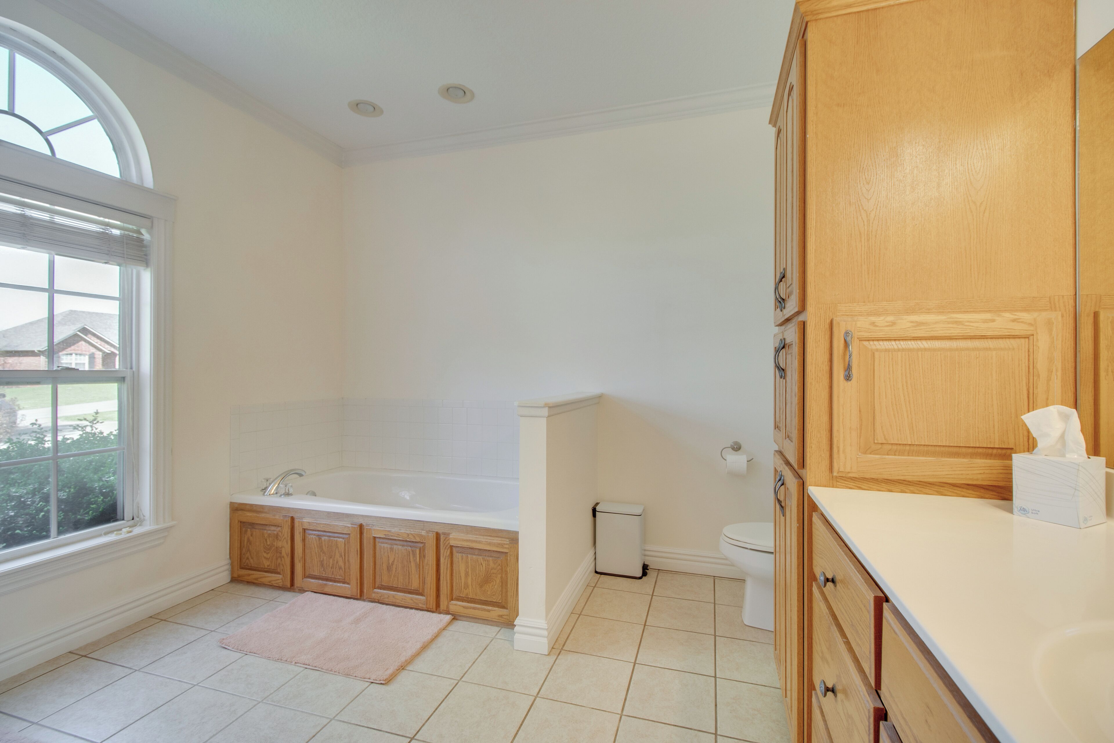 A bathroom with a bathtub, toilet, wooden cabinets, and a window.