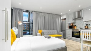 Moderni hotellihuone, jossa on sänky, sohva, ruokapöytä ja pieni keittiö.
