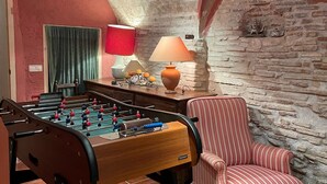 Una habitación acogedora con una mesa de fútbol, un sillón a rayas y una pared de piedra.