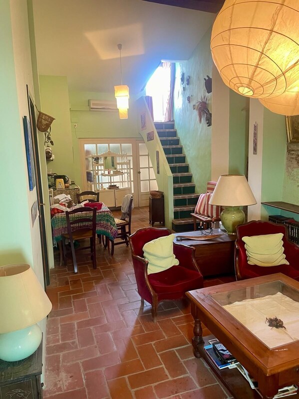 A cozy living room with a staircase, a dining area with a table and chairs, and a kitchen area with a stove and sink.