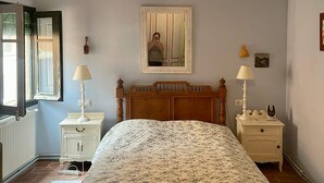 Un dormitorio con una cama, dos mesitas de noche con lámparas, un aparador, un espejo y una ventana con persianas.