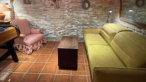 Una habitación acogedora con pared de piedra, un sofá amarillo, una silla a rayas y una pequeña mesa de madera.