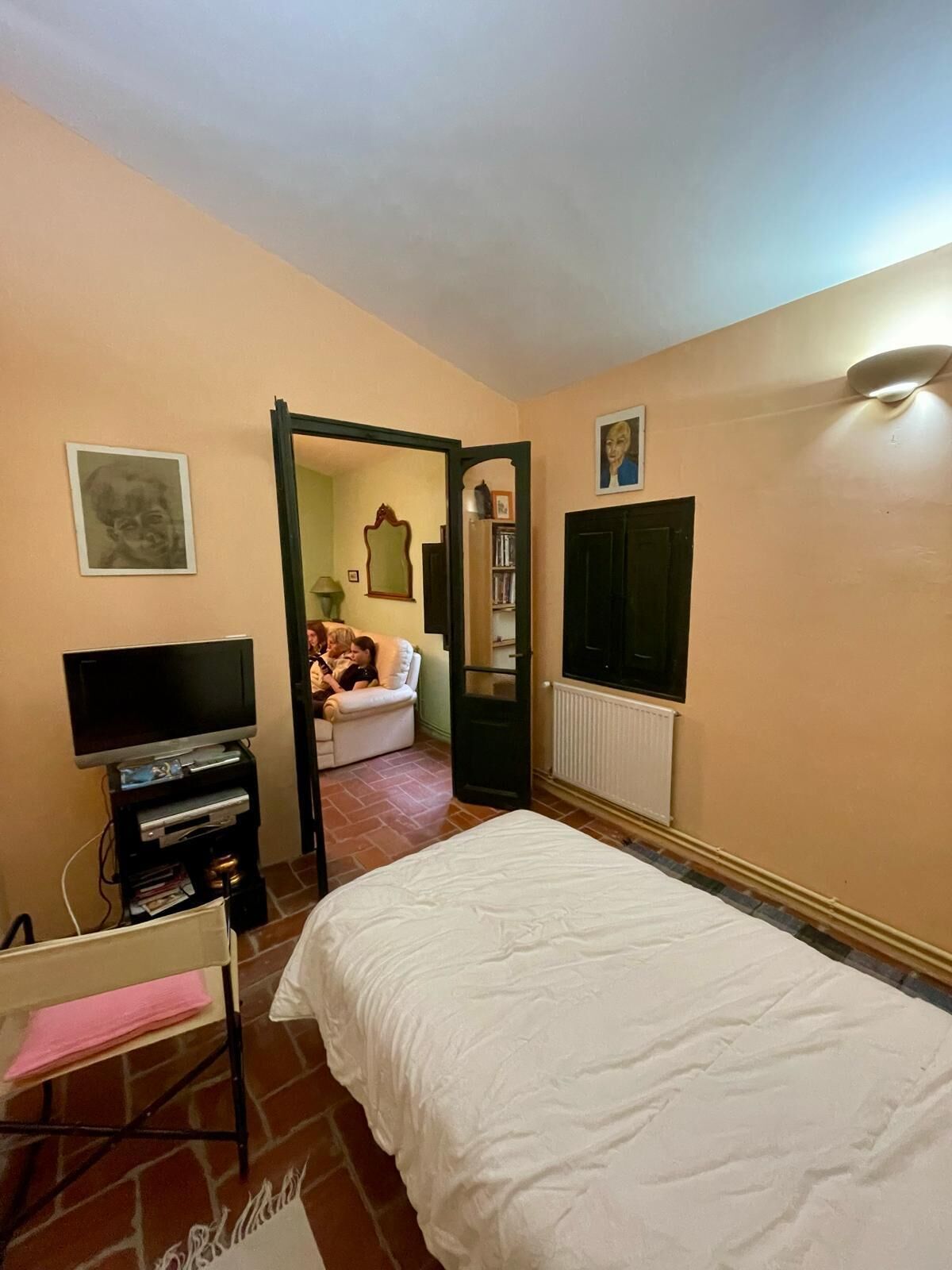 A bedroom with a bed, a television, a dresser, and a door leading to another room.