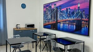 A modern room with a large cityscape painting, a clock, a kitchenette, and a seating area with tables and chairs.