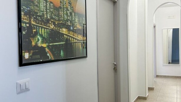 Un couloir orné d’un tableau représentant un paysage urbain encadré, avec un interrupteur et une porte donnant sur une autre pièce.