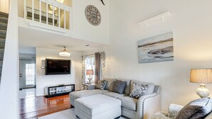 A spacious living room with a large sectional sofa, a flat-screen TV, a chandelier, and a painting on the wall.