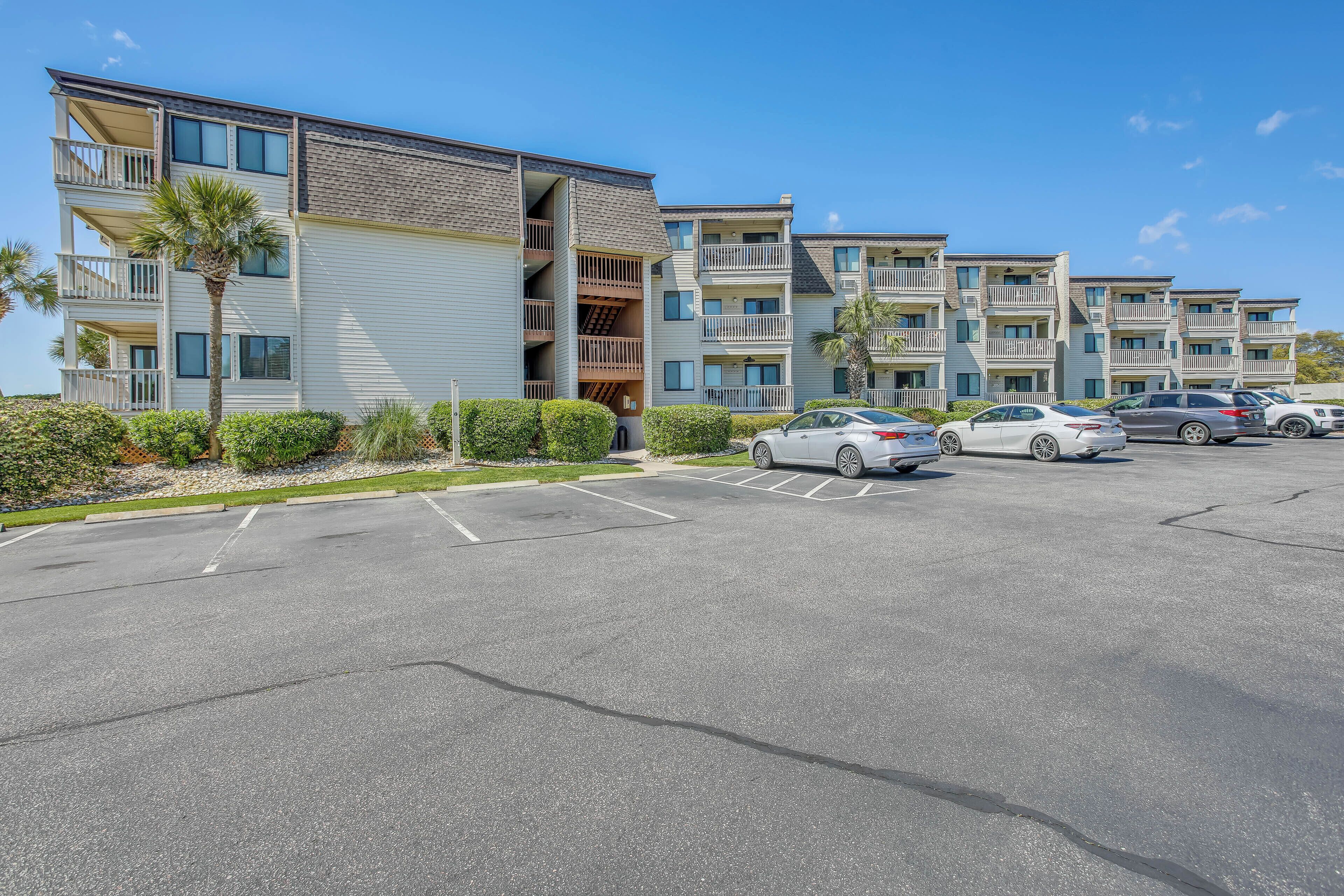 A multi-story residential building with balconies, a parking lot, and several cars.
