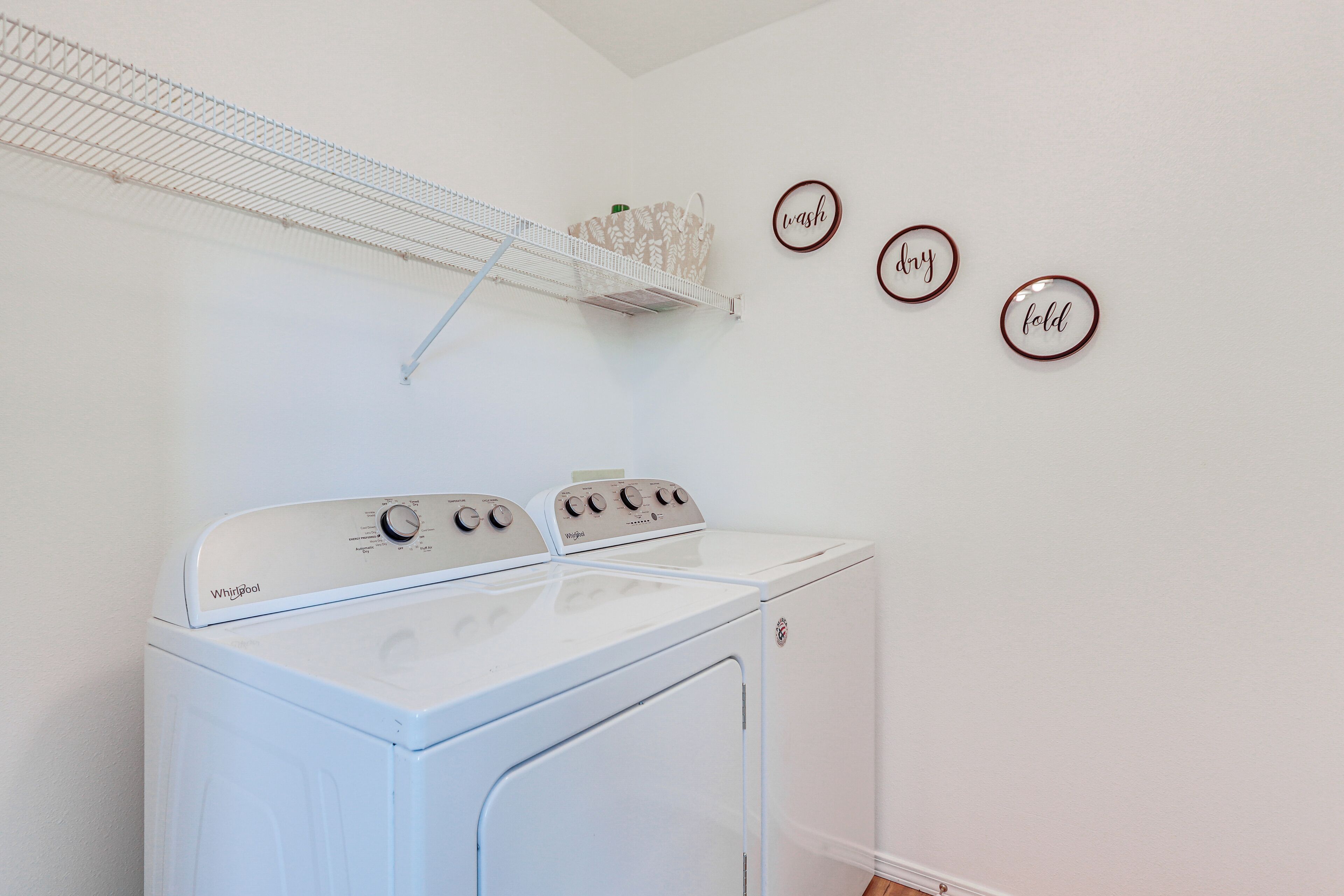 A laundry area with a Whirlpool washer and dryer, a drying rack, and three wall-mounted signs reading "wash," "dry," and "fold."