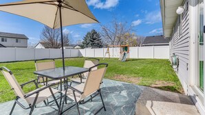 Un patio con mesa y sillas, un paraguas grande y vistas a una casa y jardín.