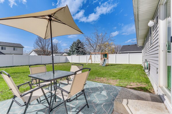 Un patio con mesa y sillas, un paraguas grande y vistas a una casa y jardín.