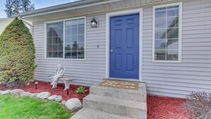 Una casa con puerta azul, un banco y un jardín delantero bien cuidado con mulch y rocas.