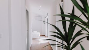 Un pasillo moderno de hotel con suelo de madera, paredes blancas y una cama a lo lejos.