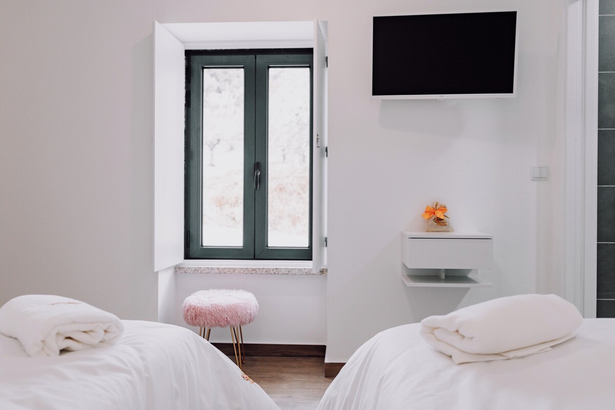 Una habitación de hotel con dos camas, una ventana con vistas, un televisor montado en la pared y un pequeño estante con un adorno.
