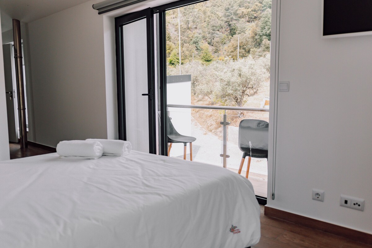 Un hotel moderno con una cama grande, un balcón con mesa y sillas, y vistas del paisaje circundante.