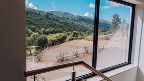 Vista desde una ventana con baranda de metal, sobre un paisaje montañoso con vegetación escasa y un sendero de tierra.