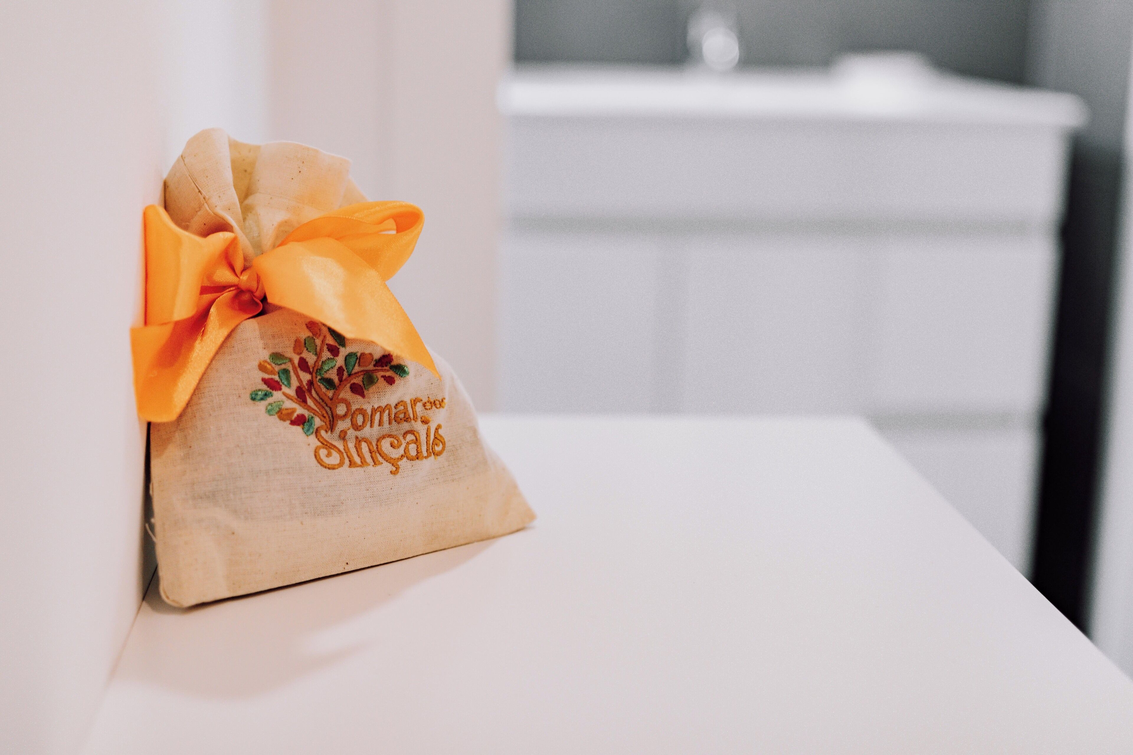 A small gift bag with a yellow ribbon and embroidered text on a white surface.