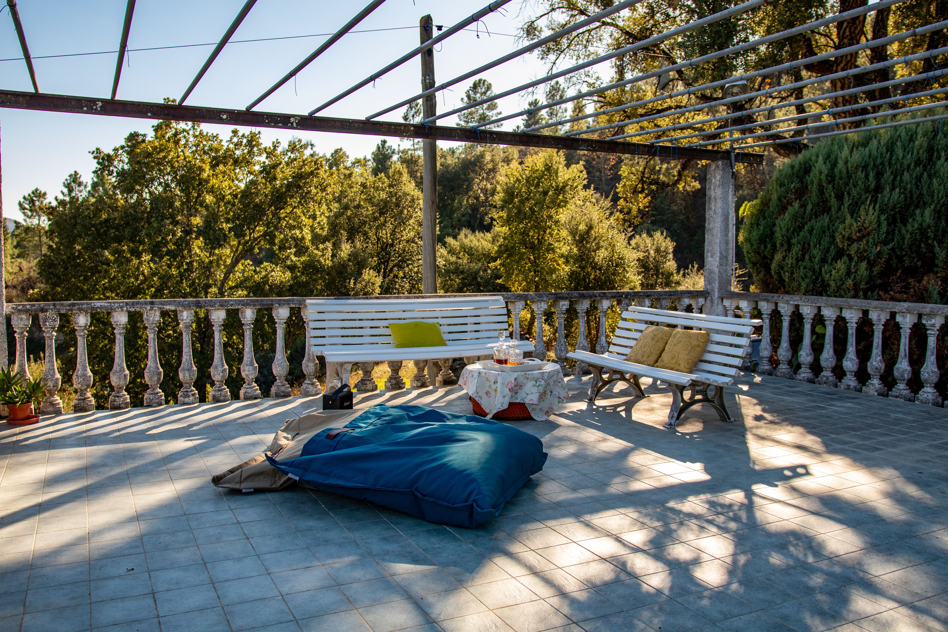 An outdoor patio with a bench, a table with a drink, and a blue bag on the floor.