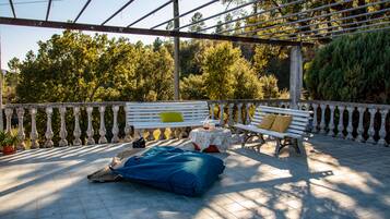 An outdoor patio with a bench, a table with a drink, and a blue bag on the floor.