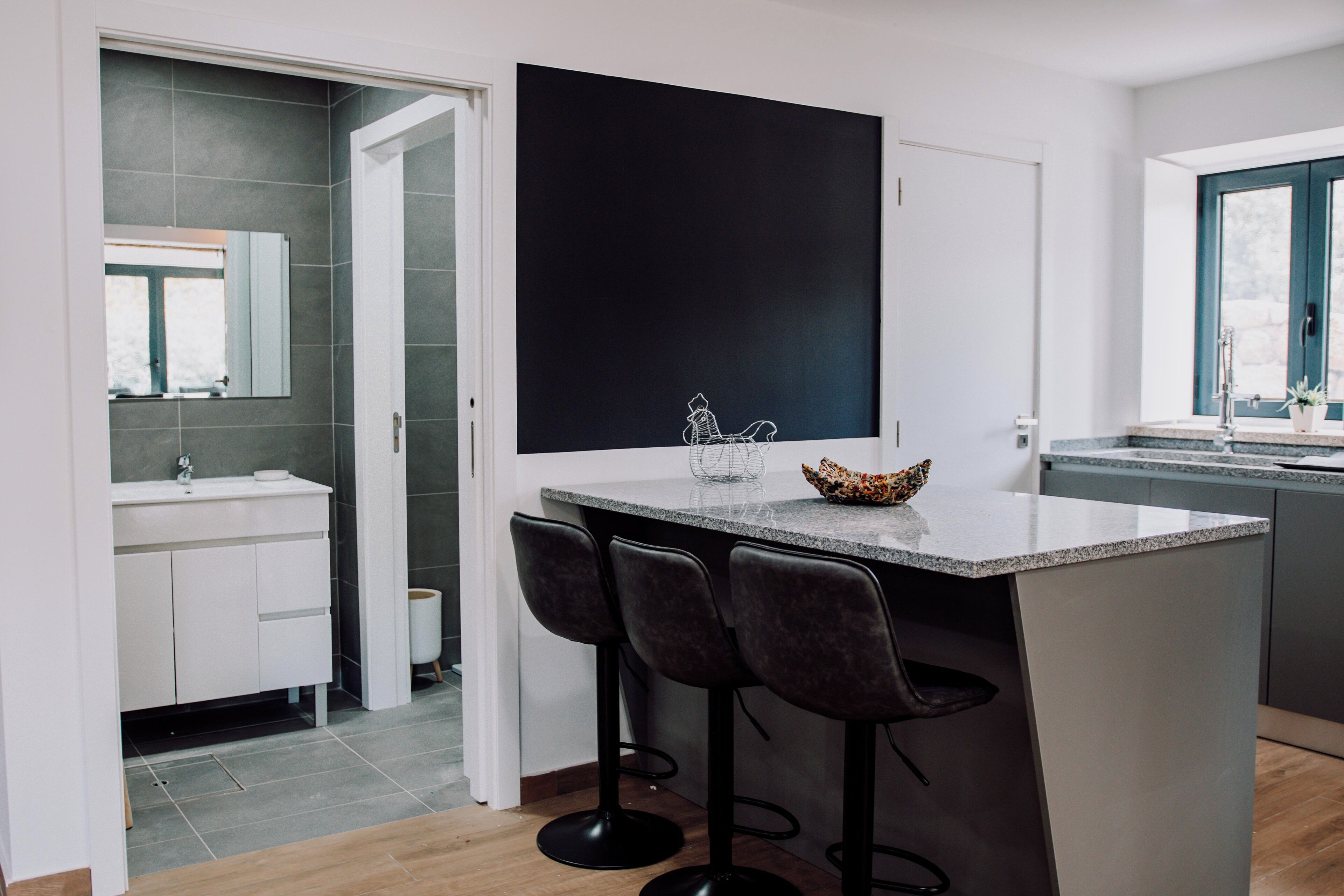 A modern kitchen with a central island, bar stools, a large black artwork, and a window with a view.