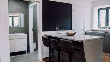 A modern kitchen with a central island, bar stools, a large black artwork, and a window with a view.