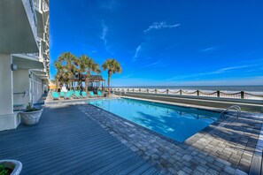 A pool area with lounge chairs and palm trees, overlooking the ocean. - 1410 Waters Edge Resort 1 Bedroom Condo by RedAwning (Murrells Inlet)