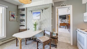 Un coin repas avec une table blanche, des chaises en bois, un luminaire suspendu et une étagère fixée au mur où sont pliés des draps et des serviettes.