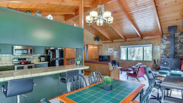 A spacious kitchen with modern appliances, a dining area with a green-tiled table, and a stone fireplace. - Cozy Cabin in Pine Mountain Lake Near Yosemite! (Groveland)