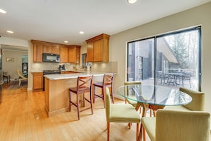 A modern kitchen with wooden cabinets, a glass island, and a dining area with a glass table and chairs. - Bloomfield Retreat w/ Pool: 6 Mi to Riverside Park (Bloomfield Hills)