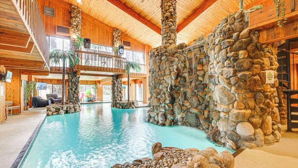 En rummelig swimmingpool indendørs med stenvæg og træloft.