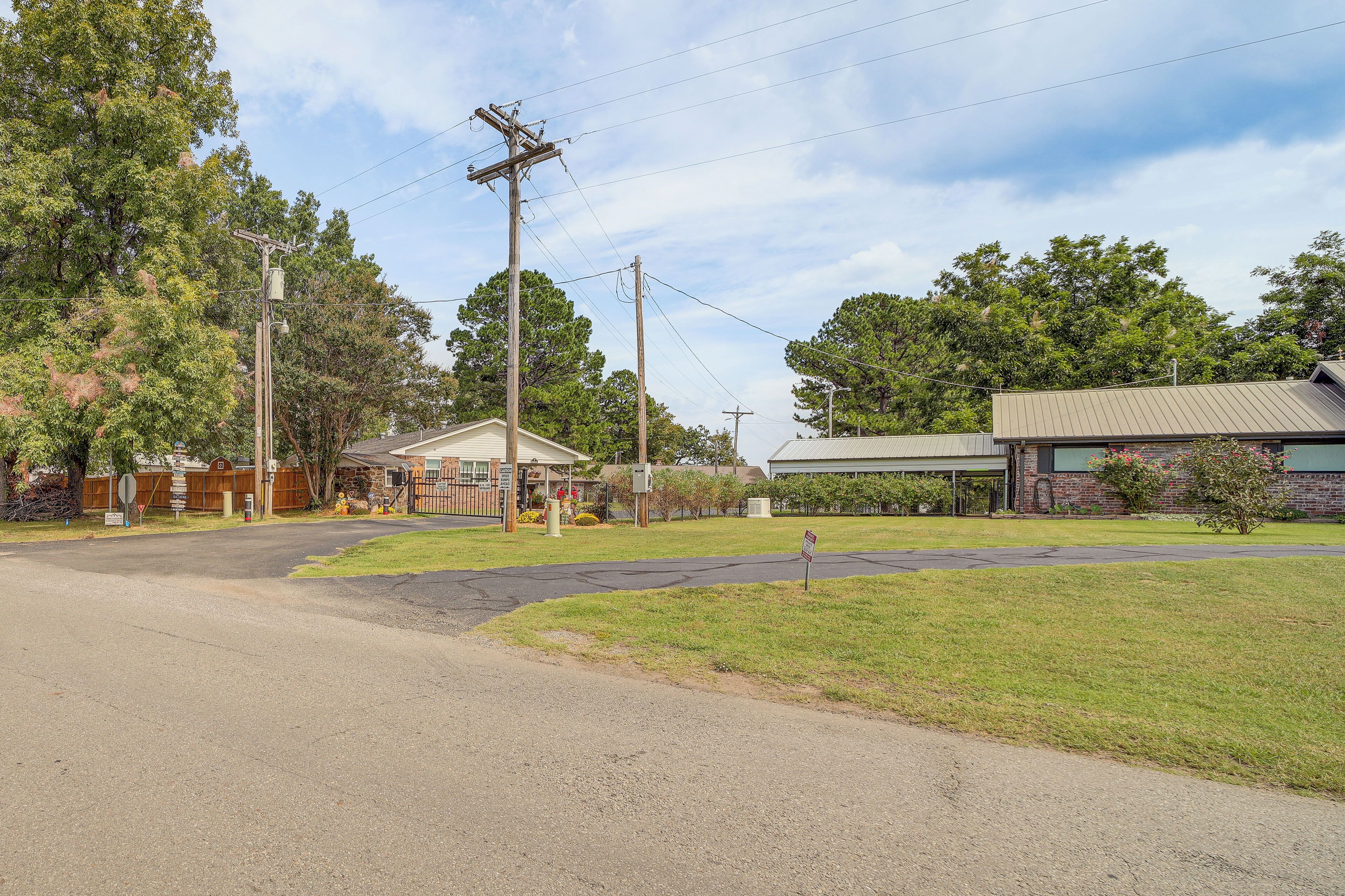 A suburban street with a grassy area, a building with a metal roof, and utility poles.