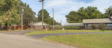 A suburban street with a grassy area, a building with a metal roof, and utility poles.