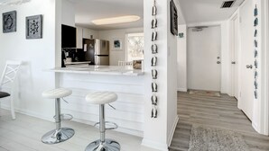 Una cocina moderna con armarios blancos, un refrigerador de acero inoxidable y una barra con dos taburetes.