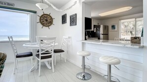 Una cocina moderna con armarios blancos, un refrigerador de acero inoxidable y un comedor con sillas blancas y una mesa redonda.