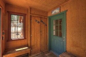 A wooden room with a bench, a green door, and a window with a view of a house.