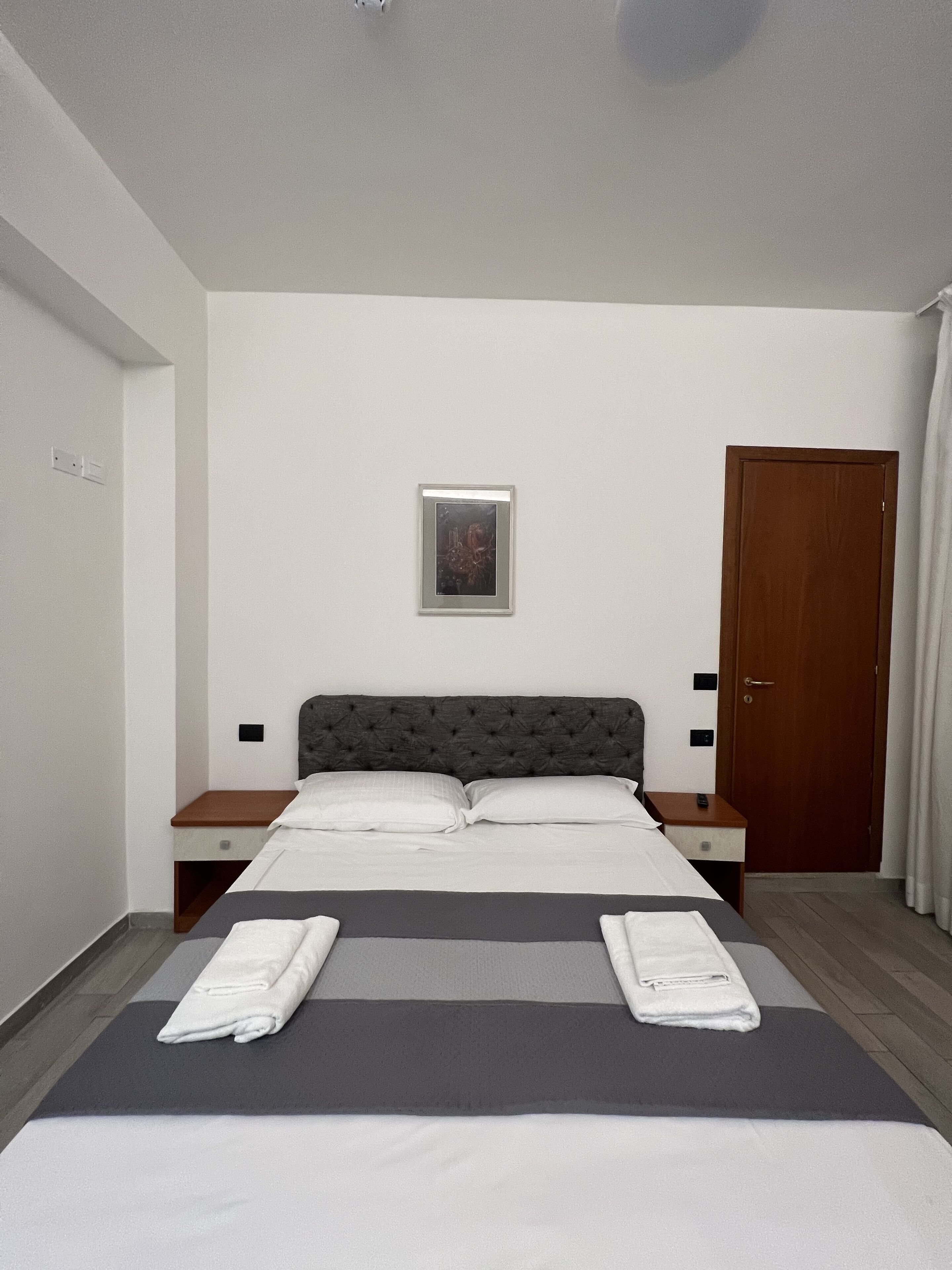 A neatly made bed with white and gray linens, a dark tufted headboard, and two bedside tables with lamps.