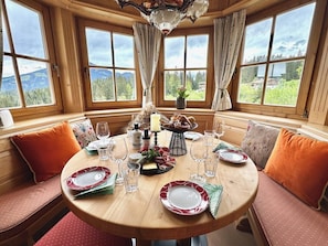 A dining area with a round wooden table set for four, surrounded by wooden benches with orange cushions. - Traumhaftes Luxus-Chalet für 8 Personen zwischen Kitzbühel & Ellma (Schattseite)