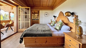 Een slaapkamer met houten vloer, een bed, een dressoir en een groot raam.