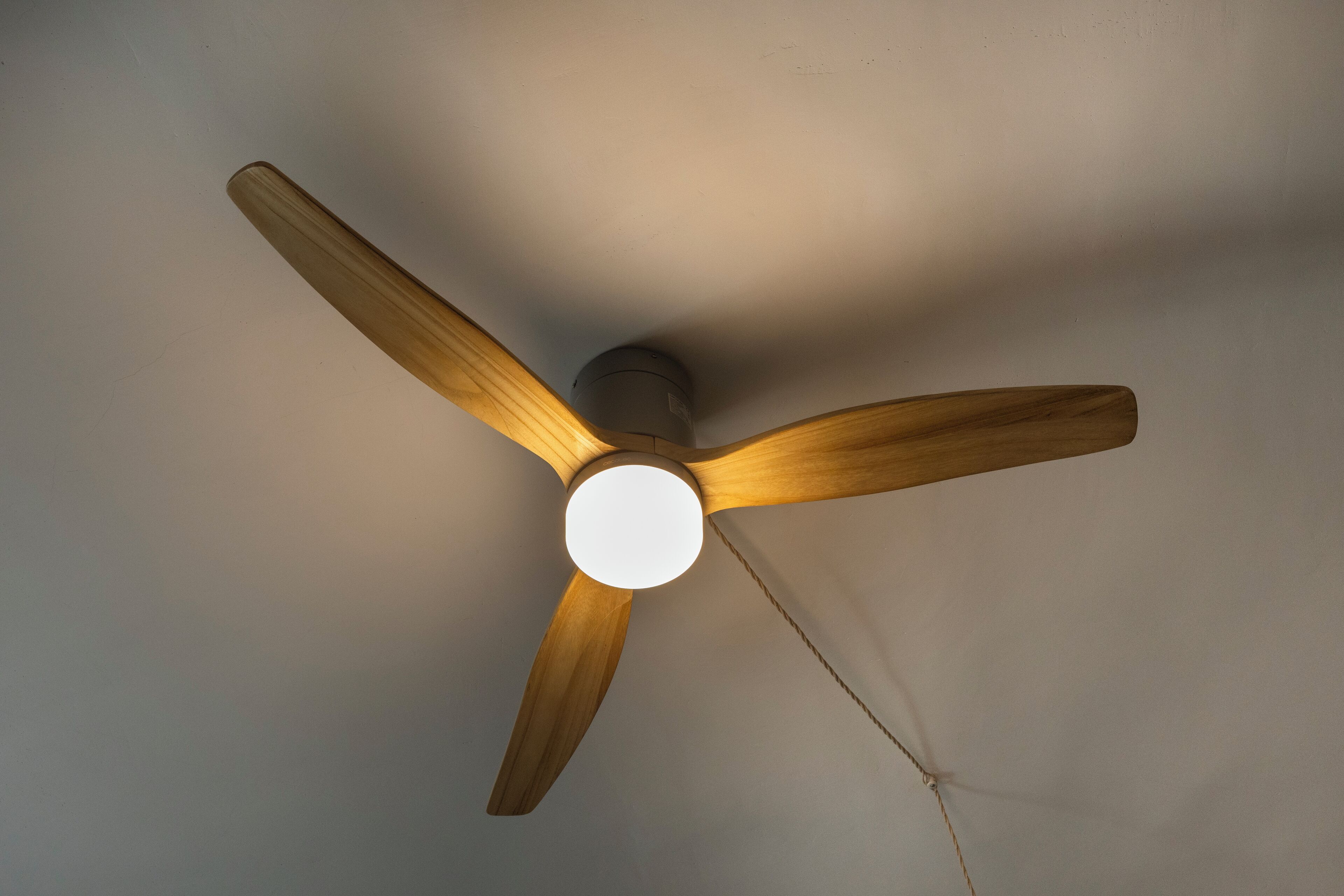 A ceiling fan with three wooden blades and a central light fixture.