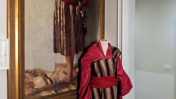A room with a large framed painting on the wall, a mannequin dressed in a striped garment, and a wooden floor.