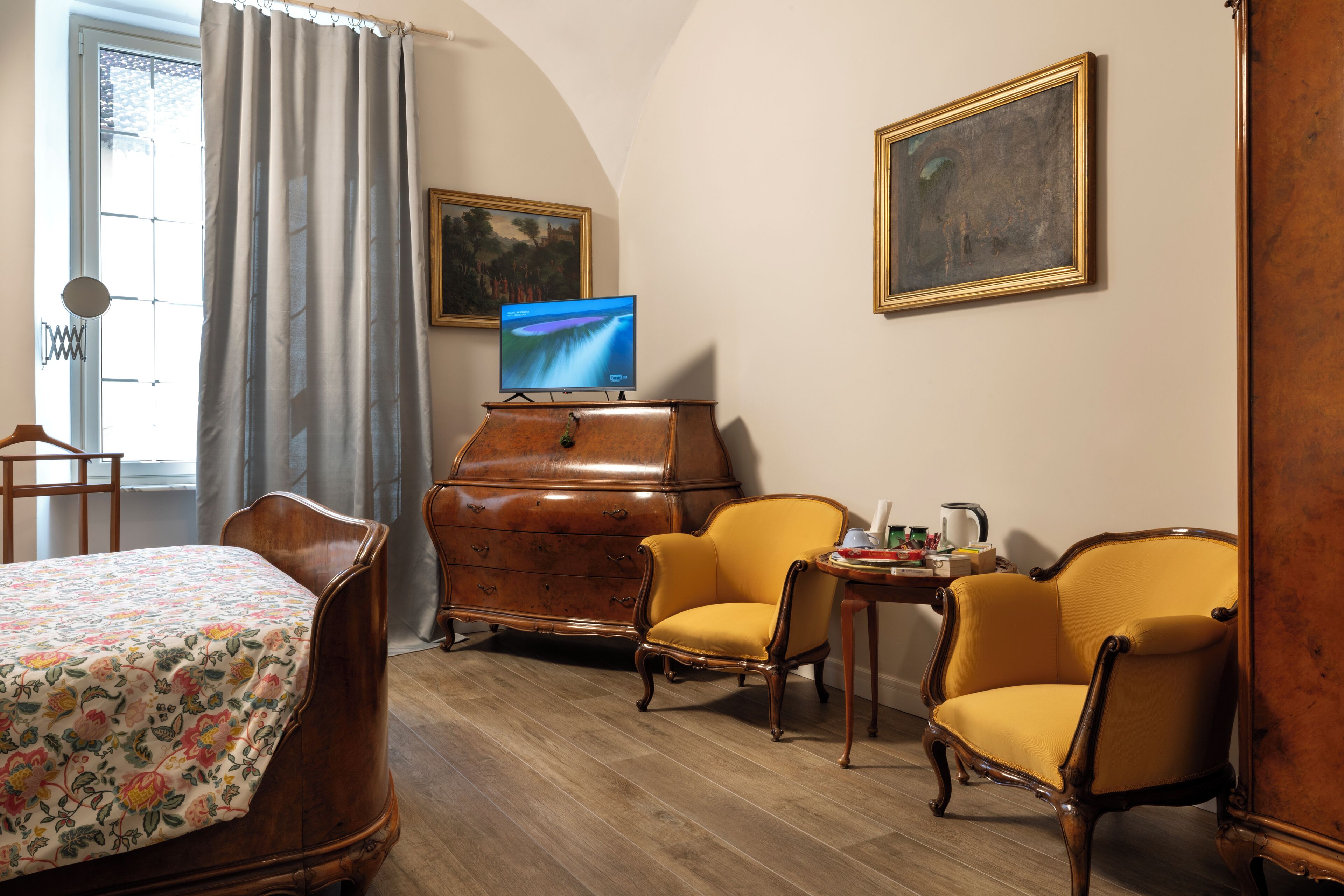 Una stanza con un letto, due poltrone gialle, un comò di legno, una televisione e due quadri appesi al muro.