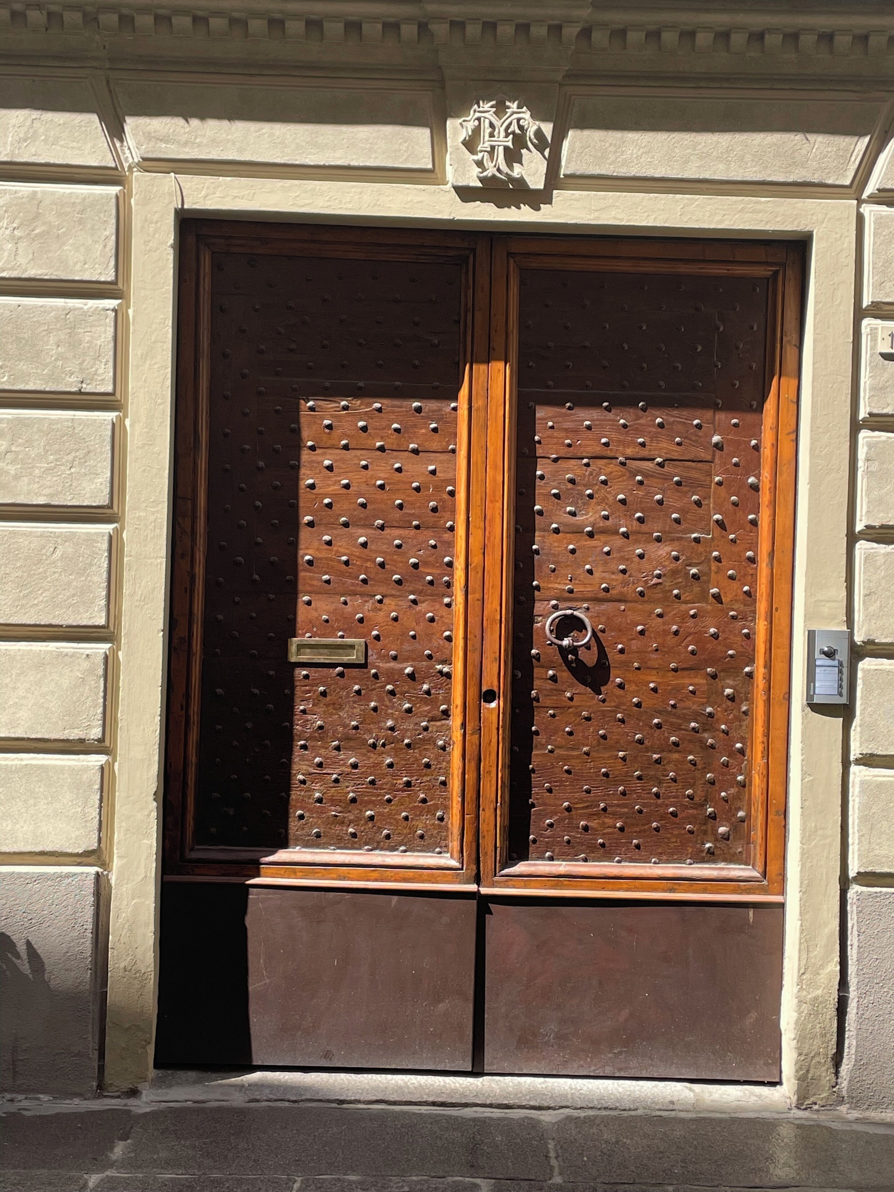 Una doble puerta de madera con un diseño de remaches metálicos, incrustada en una pared de piedra.